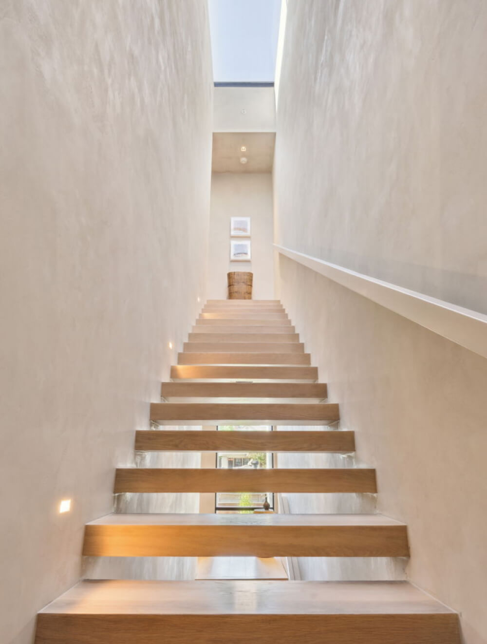 Architectural detail of open-riser stairs in blonde wood with a sleek railing, offering a modern, sculptural focal point.